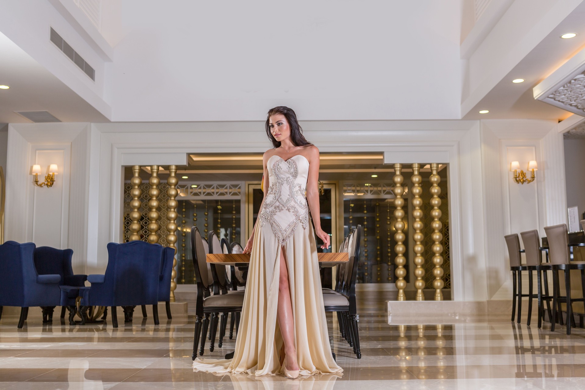 Beautiful young woman in fashion evening gown walking in luxury hotel